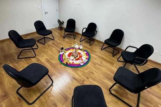 Dentro de uma sala, nove cadeiras pretas estofadas formam um círculo e, ao meio dele, estão posicionadas algumas pelúcias.