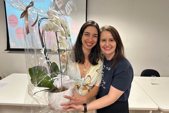 Duas mulheres posam para a foto segurando uma flor.