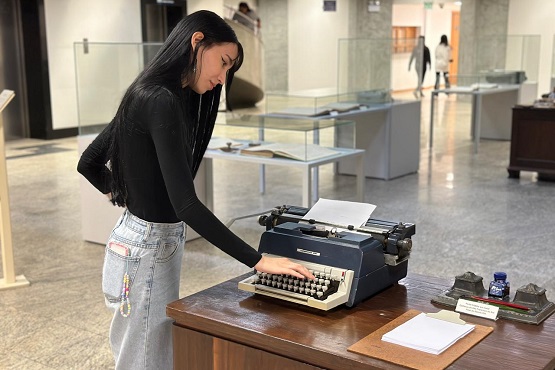 Uma mulher de pé encosta em teclas de uma máquina de escrever.