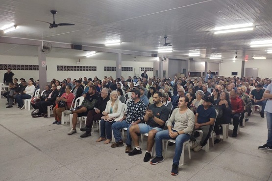 Foto tirada de pessoas sentadas em um grande salão de eventos para a entrega do programa Lar Legal.