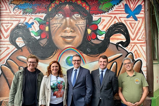 Quatro homens e uma mulher posam para a fotografia em frente a uma parede com desenhos indígenas.  