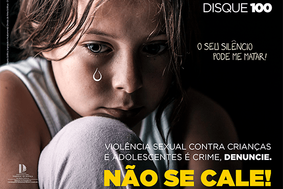 A foto mostra o rosto de um menino triste com uma lágrima desenhada no seu rosto. O texto diz: "Disque 100. O seu silêncio pode matar. Violência sexual contra crianças e adolescentes é crime, denuncie. Não se cale"