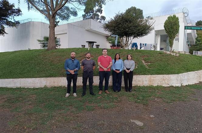 Foto colorida: grupo alinhado em área externa institucional, complexo socioeducativo, visita técnica, registrando equipe