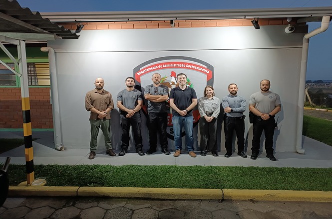 Foto colorida: grupo posando em área externa do CASE, fachada institucional ao fundo, visita técnica, registrando equipe