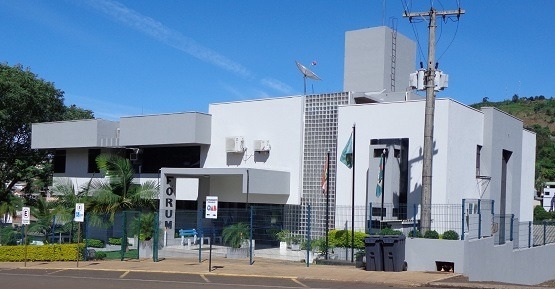 Faixada do Fórum de Quilombo. com árvores, bandeiras e um poste em frente ao prédio.