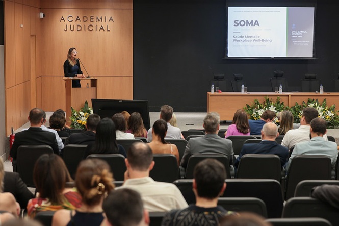 Foto colorida: palestrante ao púlpito, auditório da Academia Judicial, evento institucional, apresentando tema em bege, preto e verde