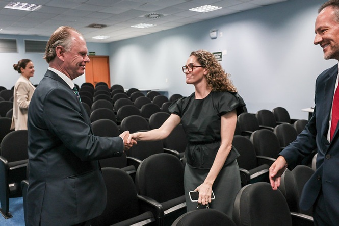 Presidente do TJ Rubens Schulz cumprimentando uma mulher de roupa preta e óculos, ambos estão  sorrindo.