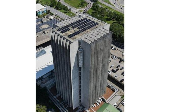 Foto horizontal: prédio do Tribunal de Justiça de Santa Catarina visto de cima, painéis solares no topo, clima de sustentabilidade e inovação.