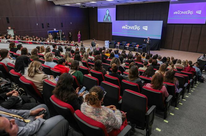 A imagem mostra um auditório cheio, com a plateia em cadeiras vermelhas assistindo a um orador no palco, diante de um telão que exibe a palavra “ANTONIETAS”.