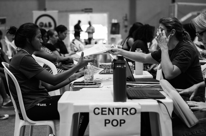 Atendimento em mesa do Centro Pop, salão interno, ação social, trocando documentos em tons preto e branco