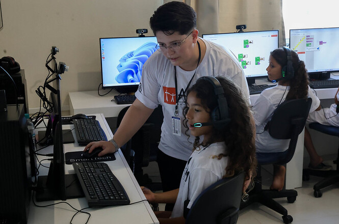Instrutor orienta criança em atividade de informática, uso de fone e computador, clima de ensino e inclusão digital