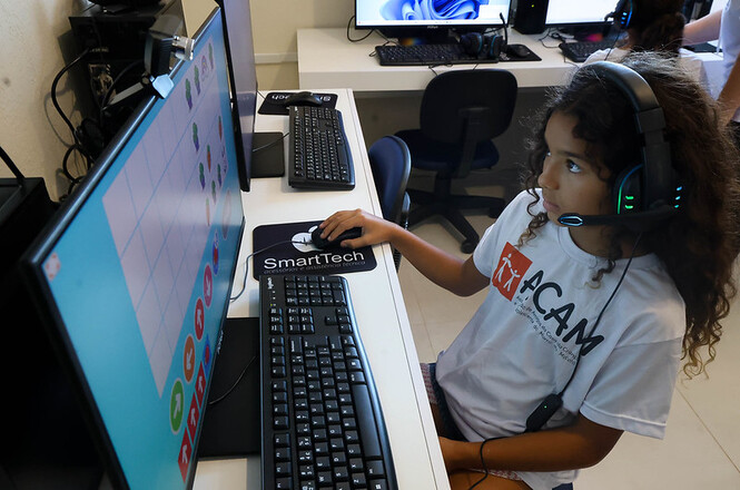 Criança usa computador com fone em atividade educativa, concentrada em programação e aprendizado tecnológico