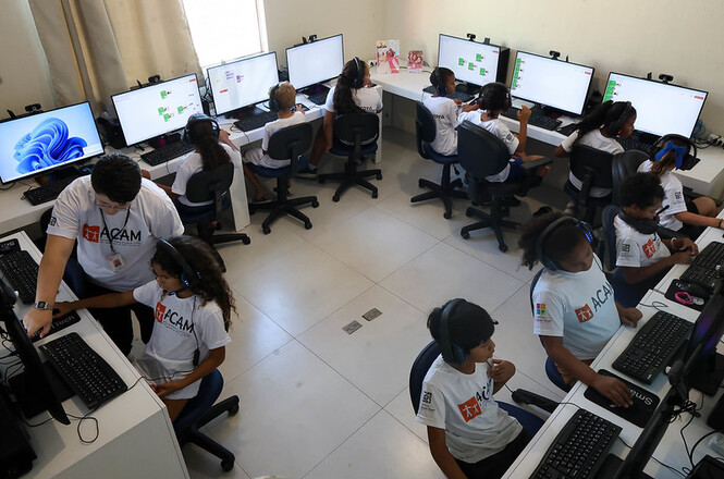 Sala de informática reúne crianças em atividade digital, com monitores e fones, ambiente de aprendizado e inclusão tecnológica
