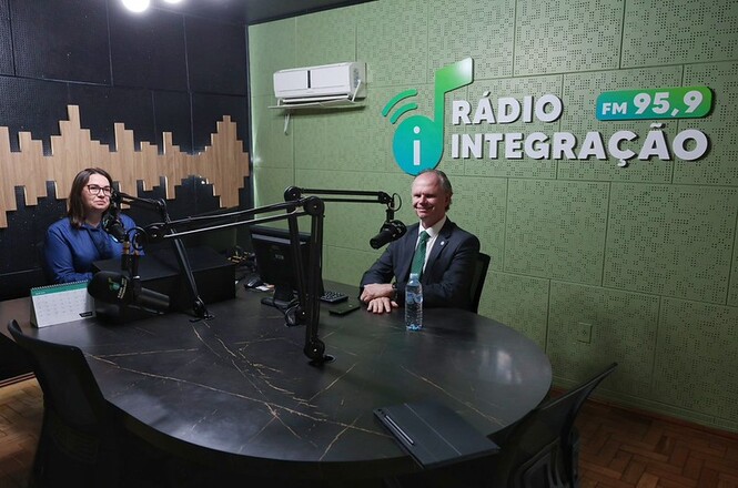 Foto horizontal: estúdio de transmissão reúne microfone, mesas de áudio, monitores e equipamentos eletrônicos.
