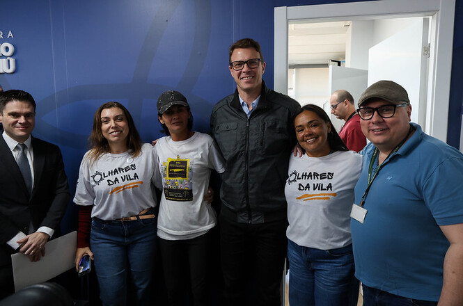 Foto horizontal: grupo posa em ambiente institucional após ação comunitária, participantes lado a lado, clima de parceria e inclusão social.