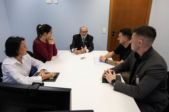 Foto horizontal: reunião de atendimento com equipe e usuários em sala, clima de escuta e orientação.