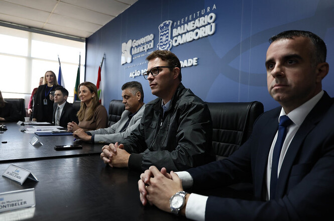 Foto horizontal: autoridades participam de reunião em sala institucional da Prefeitura de Balneário Camboriú, atentos à discussão, clima de alinhamento e cooperação.