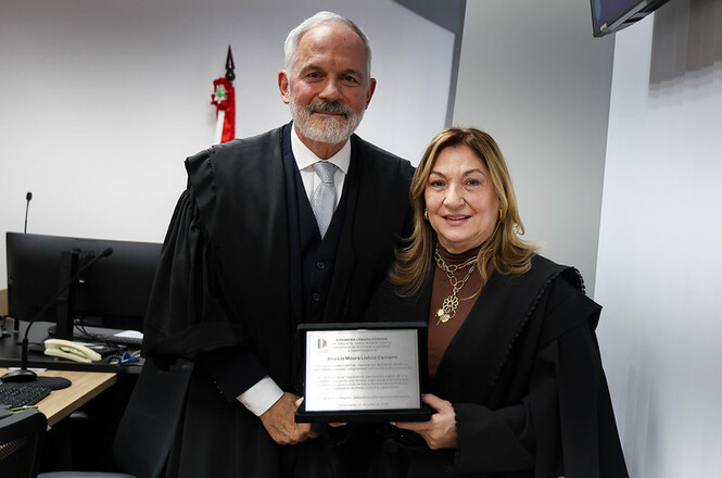 Foto horizontal: magistrada Ana Lia Barbosa Moura Vieira Lisboa Carneiro e o desembargador Carlos Alberto Civinski posam com placa de homenagem, registro institucional em destaque, clima de reconhecimento e valorização profissional.