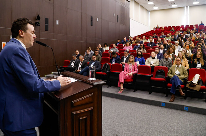 Foto horizontal: o diretor-geral administrativo do TJSC, Alexsandro Postali, discursa durante evento de capacitação na Academia Judicial, acompanhado por magistrados, servidores e convidados no auditório.