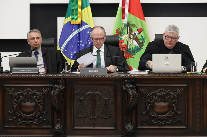 Foto horizontal: ao centro, entre as bandeiras do Brasil e de Santa Catarina, o desembargador Rubens Schulz preside sessão do Tribunal Pleno.