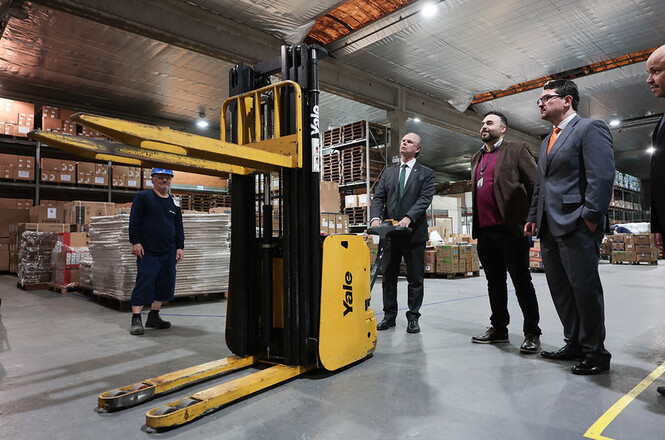 Foto horizontal: desembargador Rubens Schulz visita centro de armazenamento de materiais e observa empilhadeira ao lado de servidores.