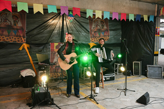 Foto horizontal: cantora e acordeonista se apresentam em palco decorado com bandeirinhas durante a festa junina promovida pelo TJSC.