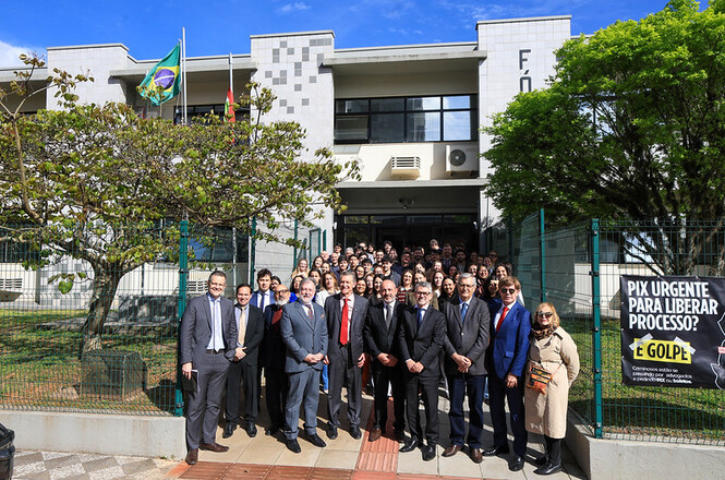 Foto horizontal: autoridades e servidores posam em frente ao fórum, com bandeiras do Brasil e de Santa Catarina.