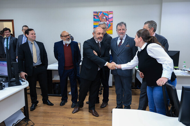 Des. André Luiz Dacol cumprimenta servidora de colete preto, diante de grupo em ambiente de trabalho.