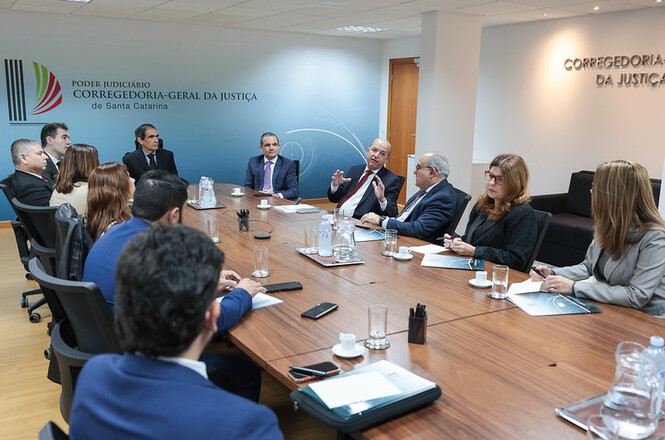 Foto horizontal: autoridades debatem em reunião na Corregedoria-Geral da Justiça, com documentos, copos e notebooks à mesa.