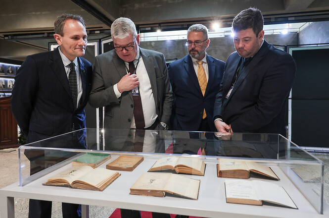 Foto horizontal: autoridades observam livros e documentos históricos dispostos em uma vitrine de vidro durante a exposição Farol da Jurisprudência do TJSC.