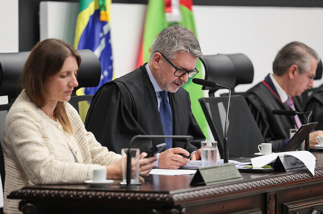 des. dinart francisco machado, ao microfone Foto horizontal: desembargador Dinart Francisco Machado fala ao microfone durante sessão no Tribunal Pleno do TJSC, com documentos sobre a bancada e magistrados ao lado.