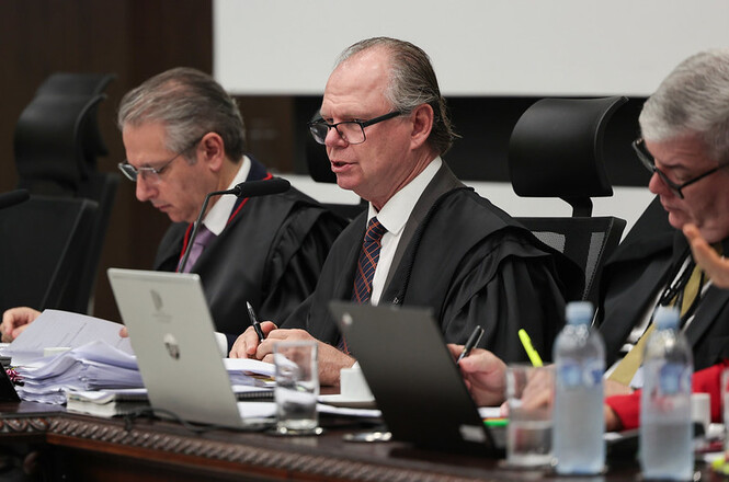 Foto horizontal: presidente do TJSC, desembargador Rubens Schulz, conduz sessão no Tribunal Pleno, acompanhado por magistrados, com processos, computadores e documentos sobre a bancada.