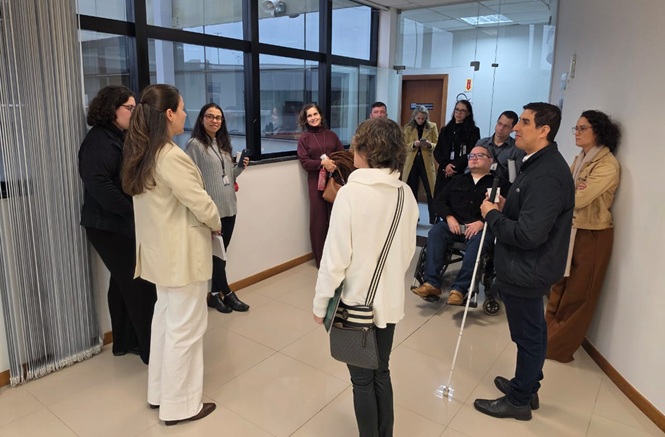 Foto horizontal: grupo conversa em ambiente interno, com participantes com deficiência visual e cadeirante.