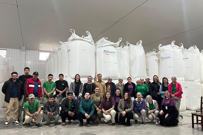 Foto horizontal: trabalhadores e participantes reunidos para registro coletivo em ambiente industrial.