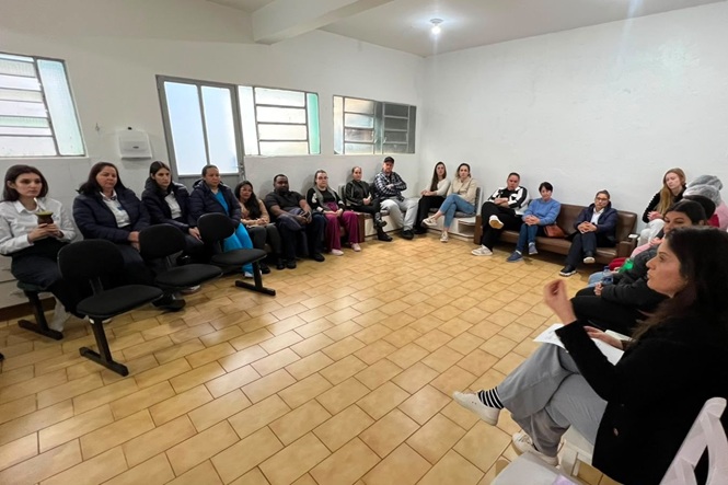 Foto horizontal: grupo participa de roda de conversa em sala, com participantes sentados em semicírculo.