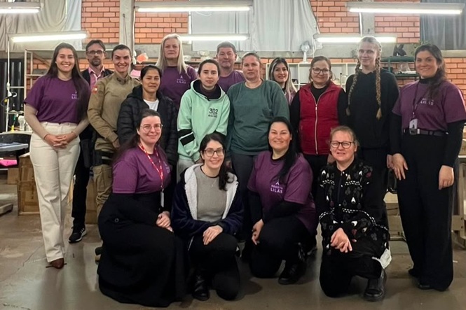 Foto horizontal: trabalhadoras e participantes reunidas para registro coletivo em ambiente industrial.