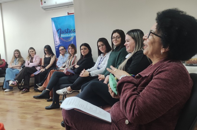 Imagem horizontal mostra mulheres reunidas em roda de conversa sobre Justiça Restaurativa durante o Agosto Lilás.