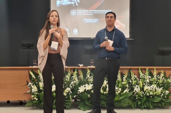Dois palestrantes no palco, auditório interno, seminário acadêmico, apresentando em preto, verde e branco