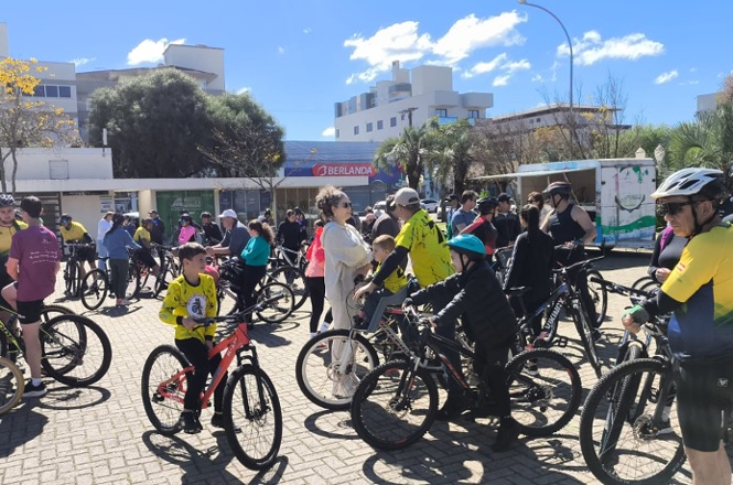 Foto horizontal: ciclistas de diferentes idades se reúnem com suas bicicletas durante passeio coletivo em área urbana.