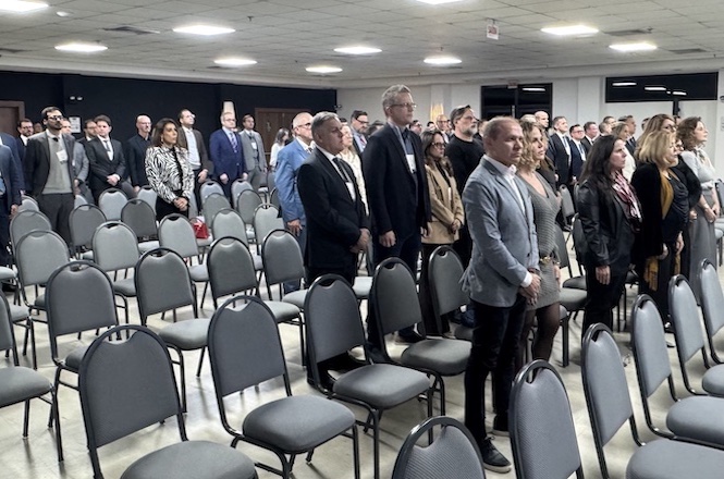 Foto horizontal: participantes do Seminário Regional da Magistratura Catarinense permanecem em pé durante solenidade de abertura realizada em auditório.