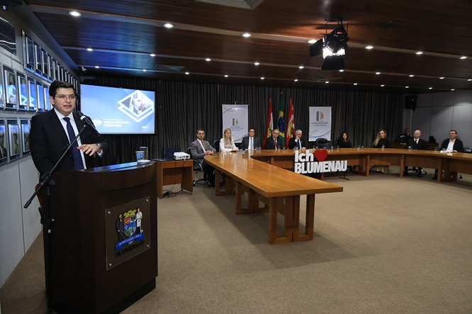 Foto horizontal: conselheiro do CNJ Marcello Terto e Silva discursa ao microfone durante evento sobre regularização tributária, diante de autoridades e convidados.
