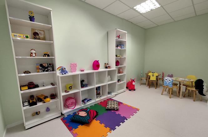 Foto horizontal: sala de acolhimento infantil com brinquedos, livros, mesas, cadeiras temáticas e espaço para atividades lúdicas.