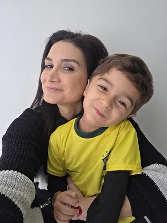 Foto vertical: mulher abraça criança com camiseta da seleção brasileira; ambos sorriem para a câmera.