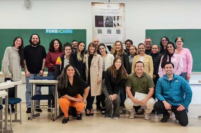 Foto horizontal: participantes de capacitação posam em sala de aula, diante de quadro verde e cartaz informativo.