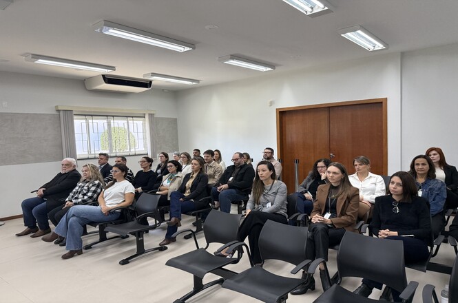 Foto horizontal: público acompanha atividade durante inspeção institucional, participantes sentados em sala observam atentamente, ambiente formal, clima de escuta e acompanhamento.