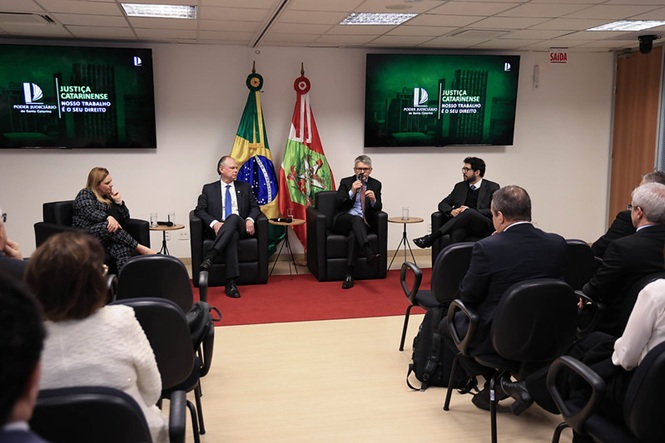 Foto horizontal: des. Dinart Francisco Machado fala ao microfone, sentado ao lado do des. Rubens Schulz, durante evento.