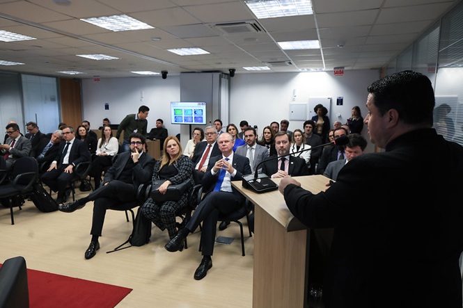 Foto horizontal: autoridade fala ao microfone em púlpito, diante de magistrados e demais participantes durante visita técnica.