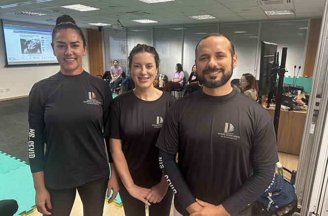 Foto horizontal: três instrutores do Poder Judiciário posam sorridentes durante curso de defesa pessoal para mulheres.