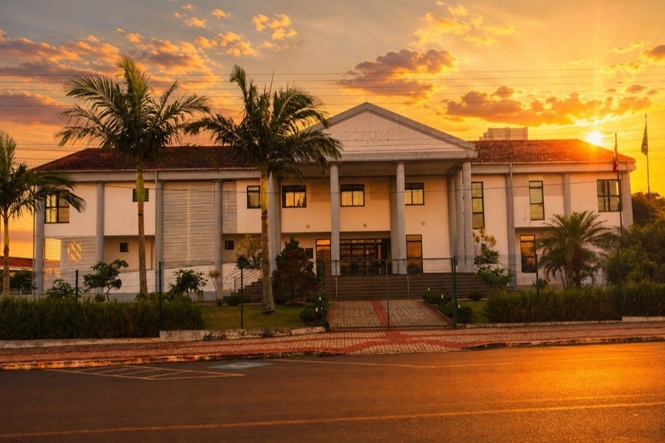 Foto horizontal: fachada do Fórum da comarca de Descanso, com colunas frontais e pôr do sol ao fundo.