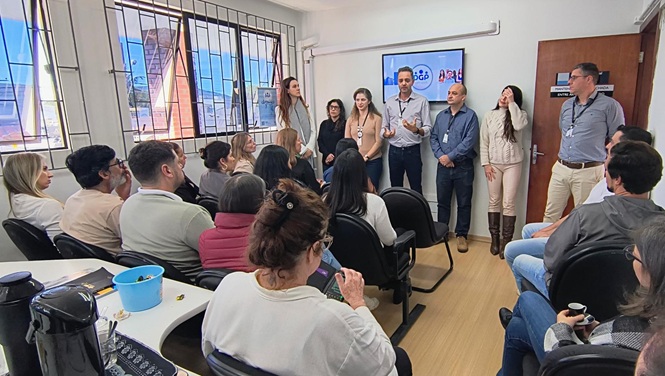 Foto horizontal: equipe apresenta projeto a grupo em sala institucional, participantes atentos, clima de troca e construção coletiva.